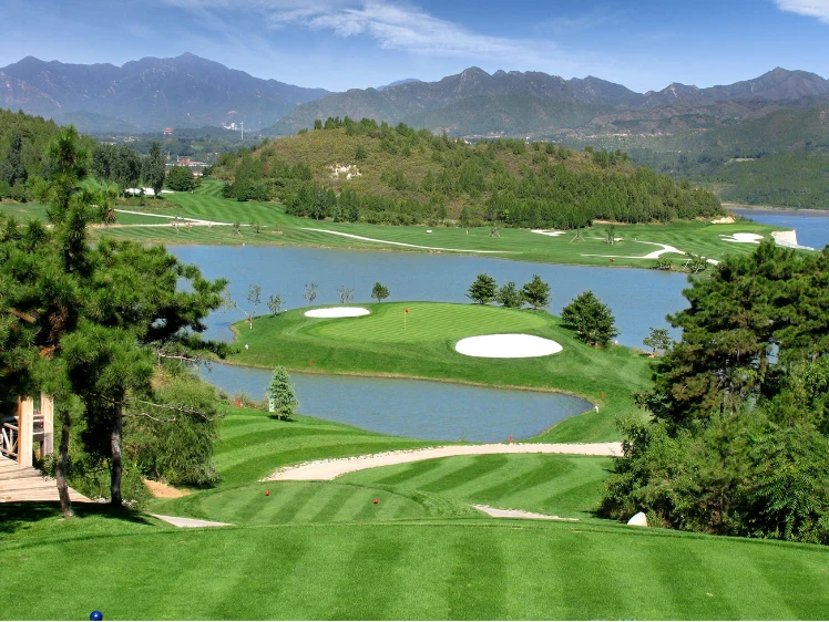 Scenic golf course with water hazards and distant mountains.