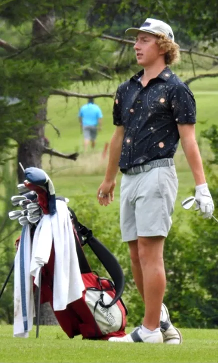 Young golfer swinging club on a lush golf course.